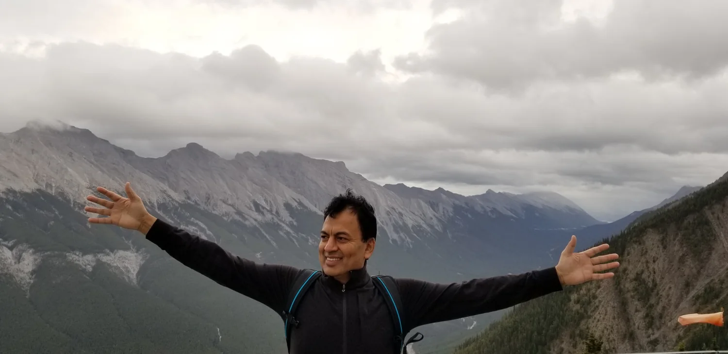 Syed Tirmizi with his arms open in front of a mountain range
